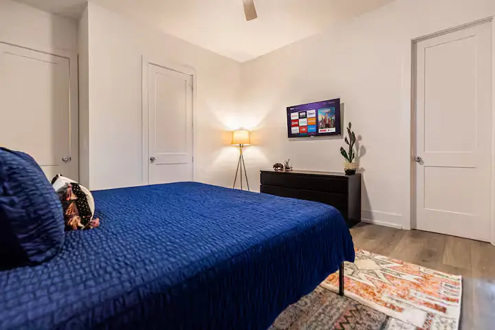 Harmony Recovery Center minimalist bedroom with blue bedding, white built-in wardrobes, wooden floors, tripod floor lamp, and clean modern design